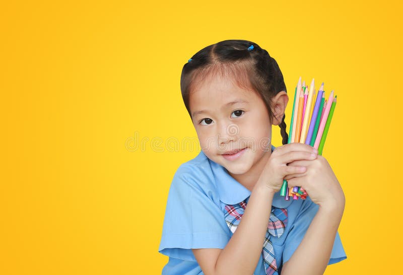 Portrait little girl in school uniform holding color pencils over yellow background. Education and school concept stock image Portrait little girl in school uniform holding color pencils over yellow background. Education and school concept stock image