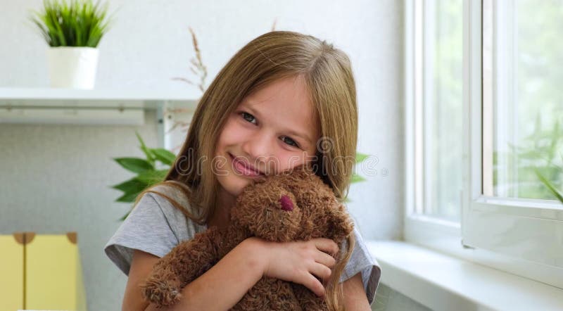 Portrait of a little girl with a teddy bear looking at camera. Smiling beautiful child hugs toy in a bright room next to royalty free stock image