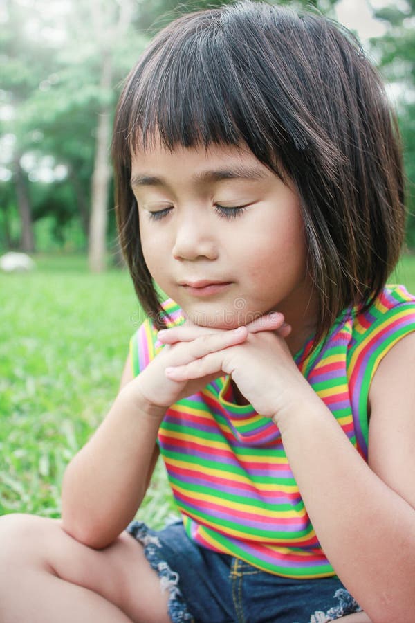 Portrait of little young asian girl praying in the spring park, Green grass background.