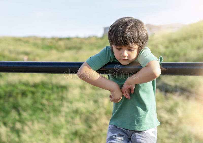 Portrait of lonely child standing alone in playground, Sad boy playing alone at the park,Poor kid with thinking face looking down