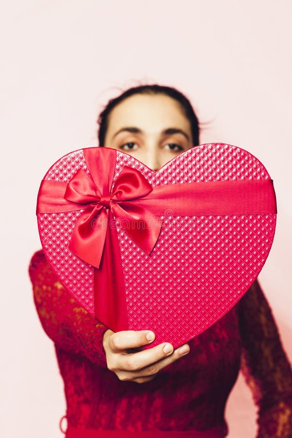 Portrait of lovely woman covering face with giftbox. Valentines day gifts. Beautiful middle-eastern girl receives heart-shaped