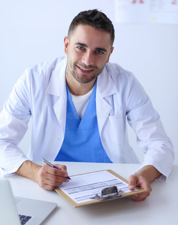 Portrait Of A Male Doctor With Laptop Sitting At Desk In Medical Office