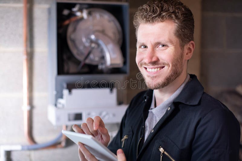 Portrait Of Male Heating Engineer Servicing Central Heating Boiler Using Digital Tablet royalty free stock photo