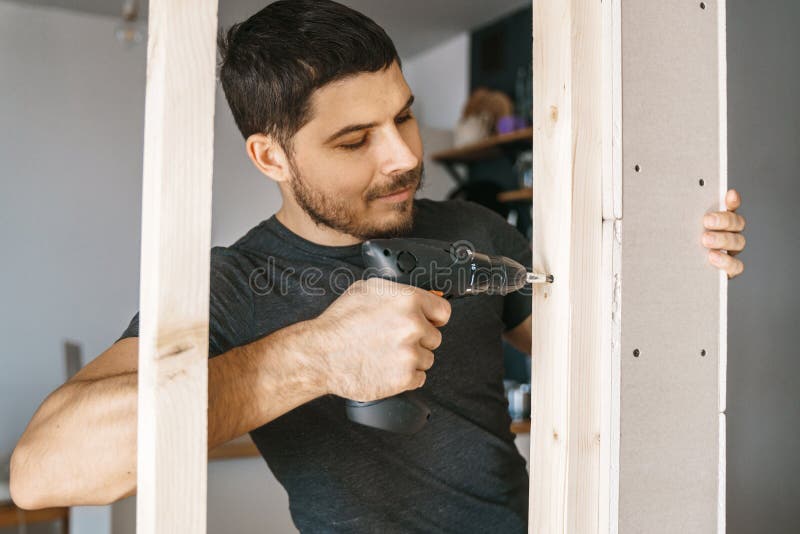 Portrait of a man in home clothes with a screwdriver in his hand fixes a wooden construction for a window in his house.