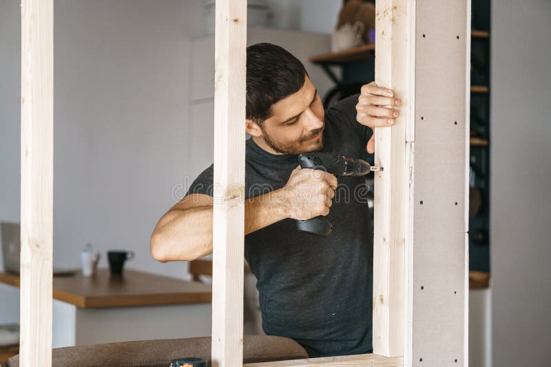 Portrait of a man in home clothes with a screwdriver in his hand fixes a wooden construction for a window in his house. Repair