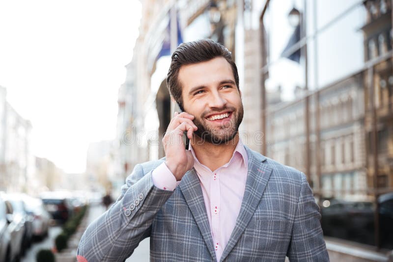 Portrait of a happy handsome man in jacket talking on mobile phone in a city area. Portrait of a happy handsome man in jacket talking on mobile phone in a city area