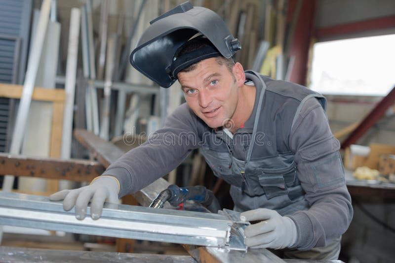 A Man Wearing a Welding Helmet Bends Down To Cut a Piece of Excess