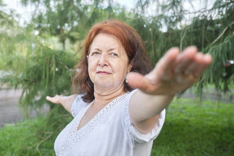 Portrait of a mature Hispanic woman in white clothes practicing yoga outdoors in a park. Concepts: wellness, balance, active and healthy lifestyle. Portrait of a mature Hispanic woman in white clothes practicing yoga outdoors in a park. Concepts: wellness, balance, active and healthy lifestyle