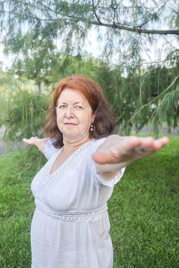 Portrait of a mature Hispanic woman in white clothes practicing yoga outdoors in a park. Concepts: wellness, vitality, active and healthy lifestyle. Portrait of a mature Hispanic woman in white clothes practicing yoga outdoors in a park. Concepts: wellness, vitality, active and healthy lifestyle