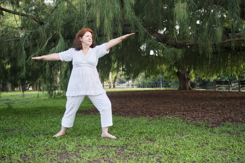 Portrait of a mature Hispanic woman in white clothes practicing yoga outdoors in a park. Concepts: wellness, vitality, active and healthy lifestyle. Portrait of a mature Hispanic woman in white clothes practicing yoga outdoors in a park. Concepts: wellness, vitality, active and healthy lifestyle