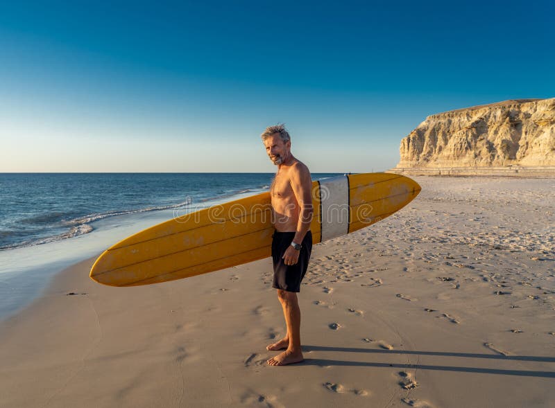 Attractive Australian mature man surfer with cool vintage surfboard on beach at sunset. Senior adult happy to be Back to surf . Outdoors sports adventure, active older people and retirement lifestyle. Attractive Australian mature man surfer with cool vintage surfboard on beach at sunset. Senior adult happy to be Back to surf . Outdoors sports adventure, active older people and retirement lifestyle