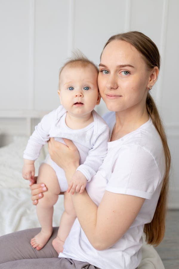 Portrait of a mother with a baby in her arms gently embracing him on a white bed at home, mother`s love