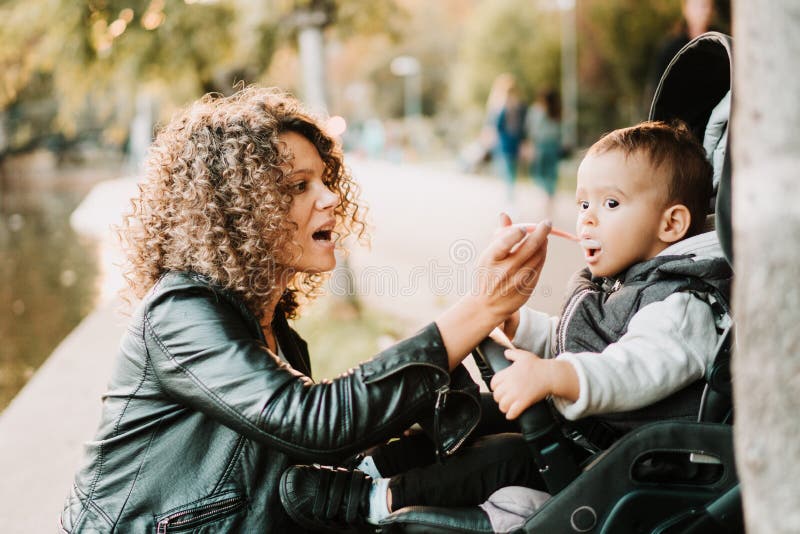 Portrait of mother feeding yogurt to 1 year old baby in stroller