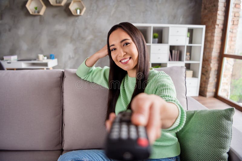 Portrait of nice charming content chinese girl sit divan watch tv switch channels remote control in house indoors