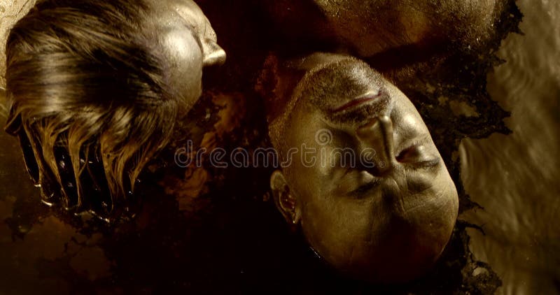 Portrait of a passionate naked wet couple: a bald men with a hairy body and a dark-haired woman, their whole body in gold pigment, skin glistening, they lie in a pool of Golden water, hugging, stroking each other. Portrait of a passionate naked wet couple: a bald men with a hairy body and a dark-haired woman, their whole body in gold pigment, skin glistening, they lie in a pool of Golden water, hugging, stroking each other.