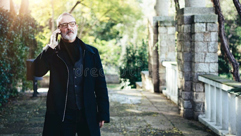Portrait of pensive adult businessman talking on his smartphone while walking in city park.Horizontal,blurred background stock photography Portrait of pensive adult businessman talking on his smartphone while walking in city park.Horizontal,blurred background stock photography