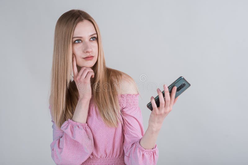 Portrait of a pensive blonde girl with a smartphone in the studio on a white background.