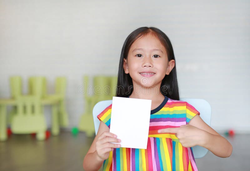 Portrait petite fille asiatique souriante tenant une carte blanche en papier dans la main en pointant Enfant affichant une note d image libre de droits Portrait petite fille asiatique souriante tenant une carte blanche en papier dans la main en pointant Enfant affichant une note d image libre de droits