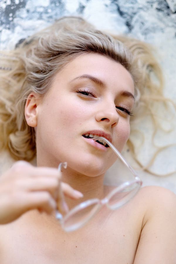 Portrait photograph of a sexy young woman with glasses and blond hair the glasses iron in her mouth