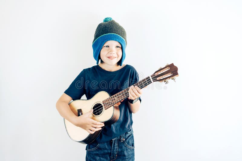 Portrait of a positive boy in casual clothes and hat playing ukulele. Copy space on white background. stock image Portrait of a positive boy in casual clothes and hat playing ukulele. Copy space on white background. stock image