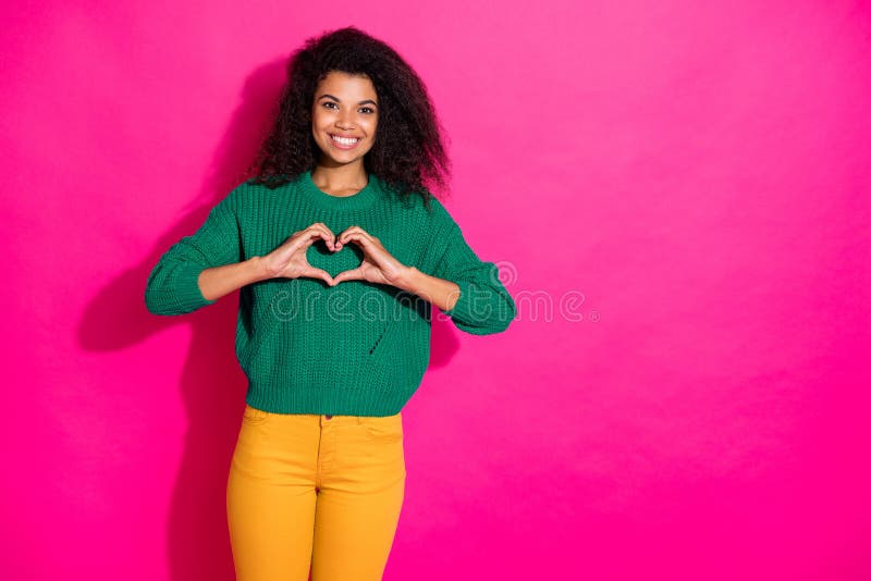 Portrait of positive dreamy afro american girl show heart from fingers, symbol of her love to boyfriend on valentine day in winter wear knitted pullover yellow pants isolated pink color background. Portrait of positive dreamy afro american girl show heart from fingers, symbol of her love to boyfriend on valentine day in winter wear knitted pullover yellow pants isolated pink color background