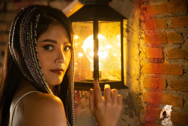 A pretty Asian woman poses and holds a lamp in the building.