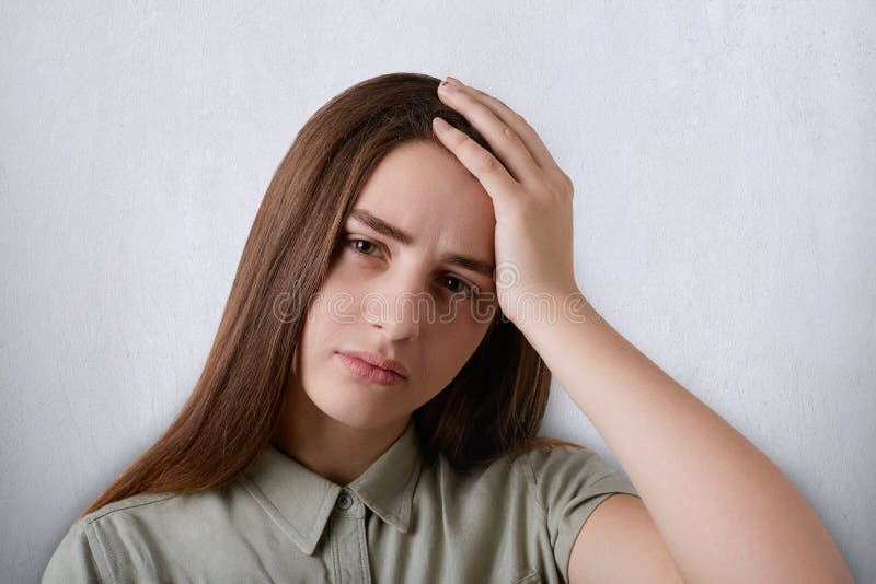 A portrait of pretty brown-eyed girl and dark long hair wearing green shirt having tired expression holding her hand on head. Youn stock image A portrait of pretty brown-eyed girl and dark long hair wearing green shirt having tired expression holding her hand on head. Youn stock image