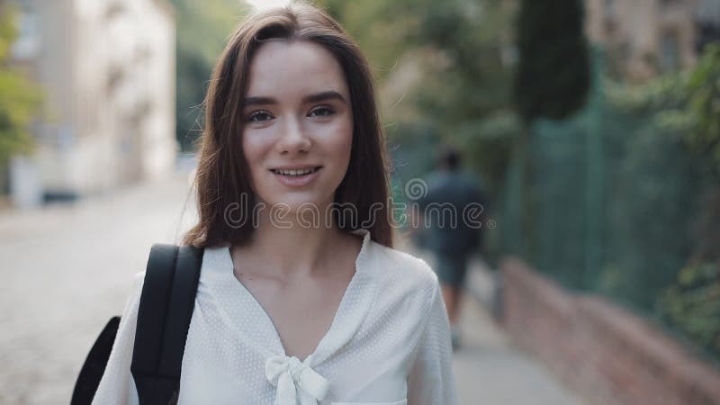 Portrait of Pretty Brunette Student Girl with a Bag Looking to Camera with a Smile. Young Woman Standing at Old City