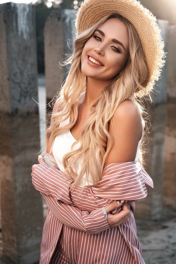 Portrait of a pretty, cute and romantic smiling girl with long loose blonde hair in a straw hat. Countryside landscape, sunlight a