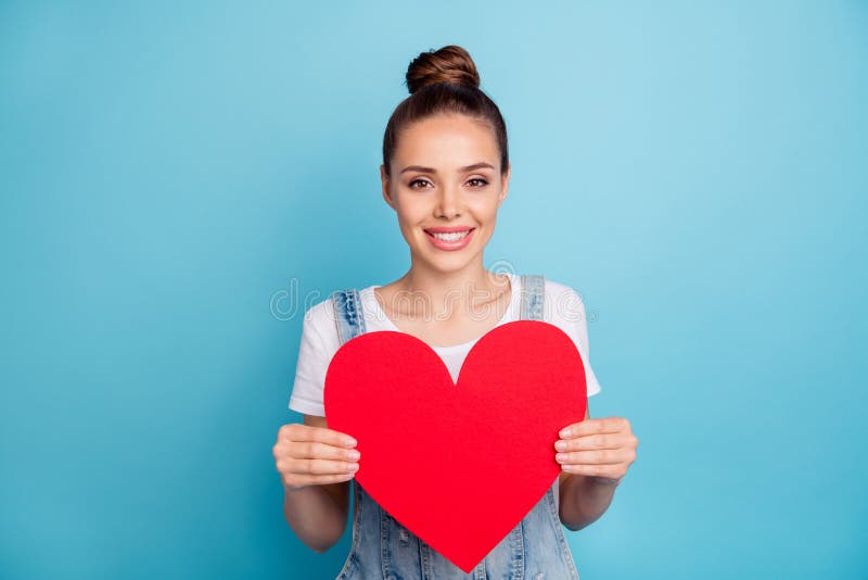 Portrait of pretty girl holding paper card gift for 14-february wearing white t-shirt denim jeans overalls isolated over