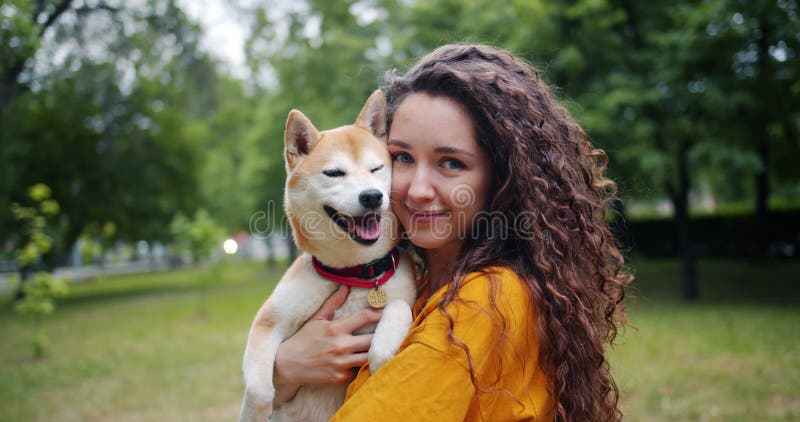 Portrait of pretty girl loving dog owner standing in park with her beautiful pet smiling