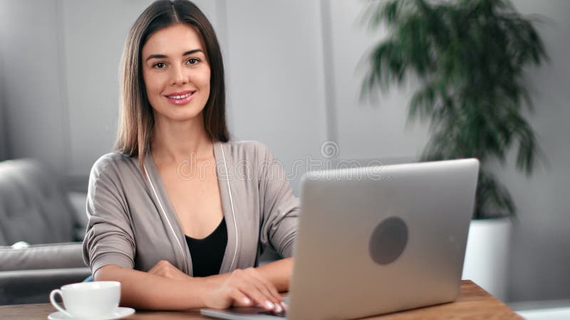 Portrait of pretty modern woman posing sitting at desk in home or office. Medium shot on RED camera