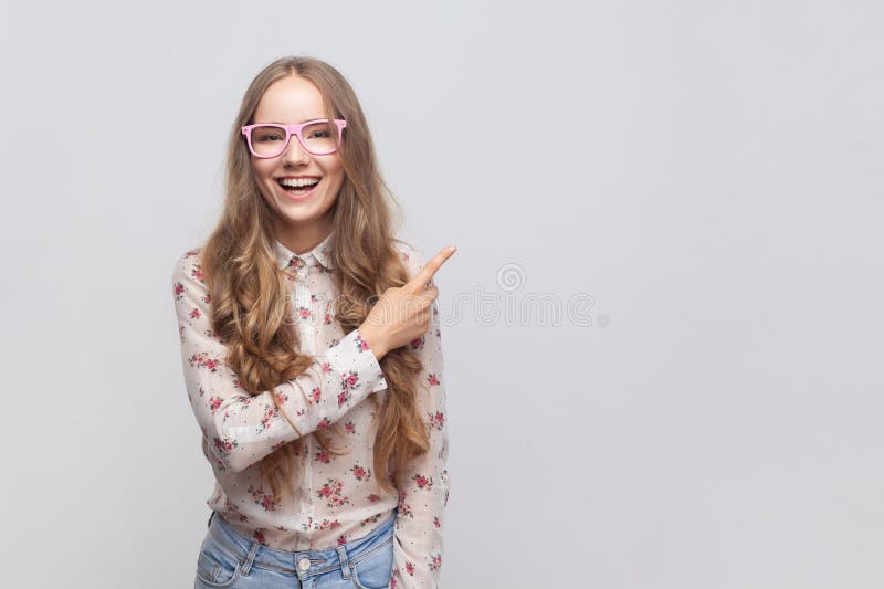 Woman pointing finger away with toothy smile on face, empty space for your advertisement. royalty free stock images