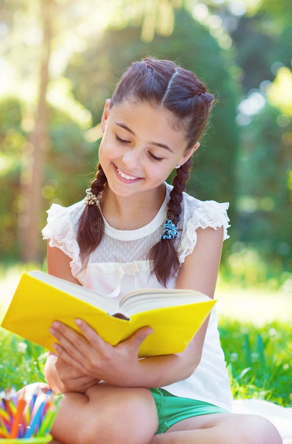 Portrait of pretty young girl reading book in park