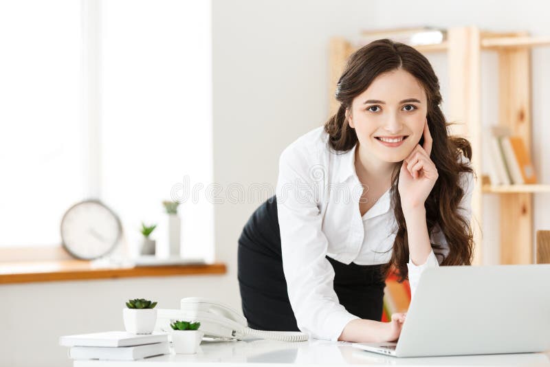 Portrait of a pretty young woman studying or working while standing with laptop computer and notebook