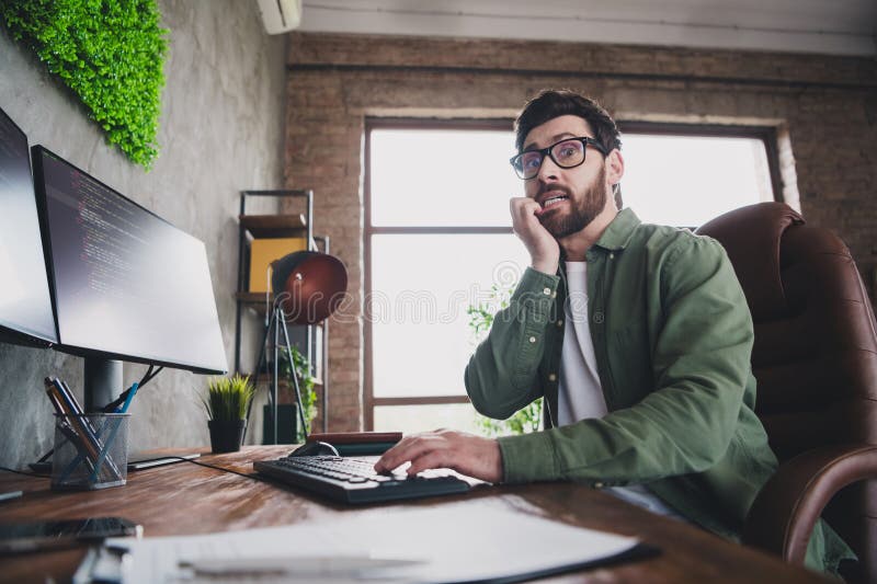 Portrait of professional hacker young man bite nails worry computer desk loft interior office indoors stock image