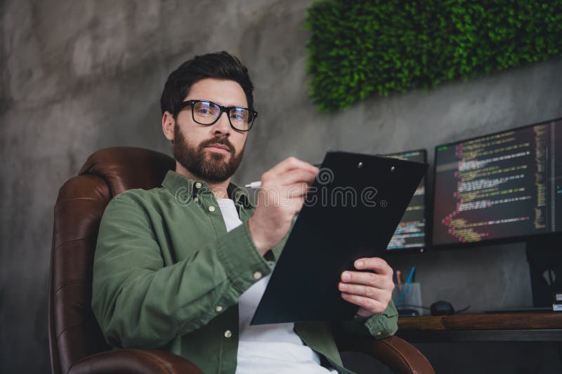 Portrait of professional hacker young man hold clipboard computer desk loft interior office indoors royalty free stock photo