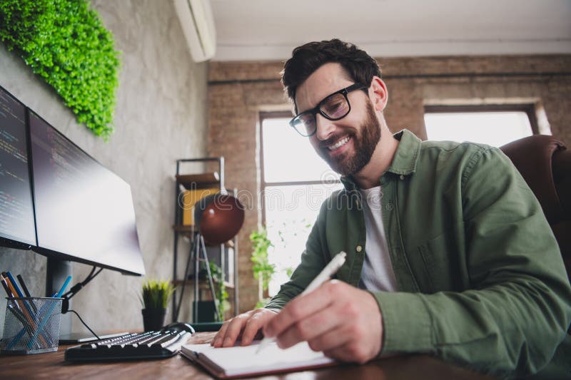 Portrait of professional hacker young man pen write notepad computer desk loft interior office indoors stock image
