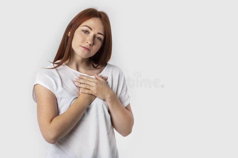 Portrait of a red-haired young woman keeps hands on chest, expresses sympathy. Kind hearted friendly nice girl shows kindness