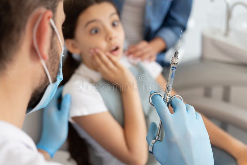 Portrait of scared girl and dentist holding syringe