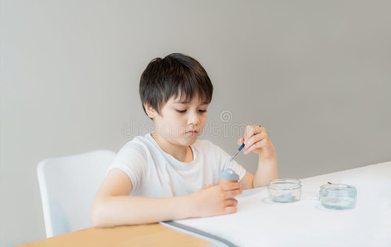 Portrait School kid using paint brushes painting grey colour on egg and DIY Easter decorations homework, Child boy preparing and stock images