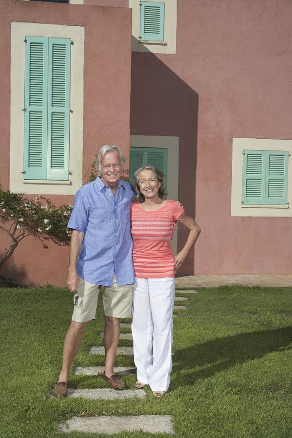 Full length portrait of a senior couple standing in front of house. Full length portrait of a senior couple standing in front of house