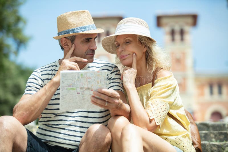 Portrait senior couple reading map while sitting on bench royalty free stock images