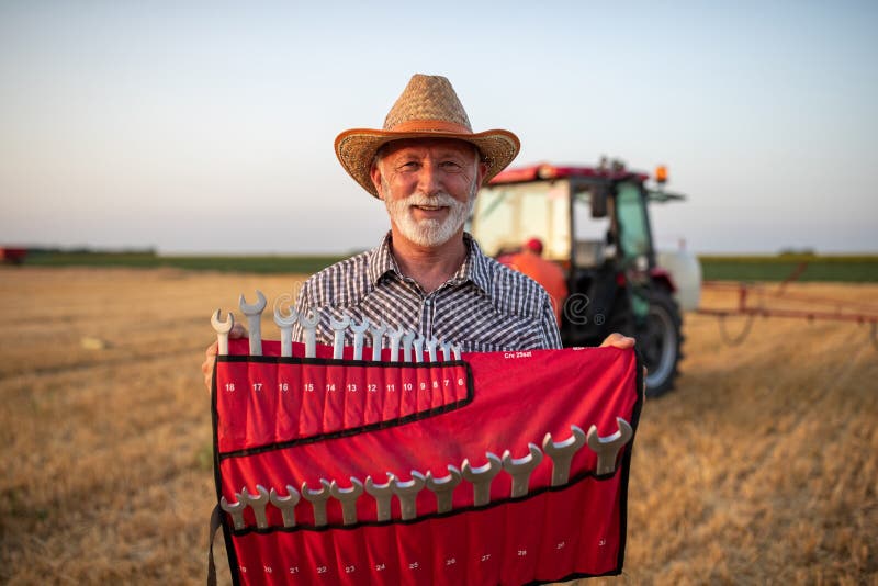 Farmer holding set of wrenches in front of tractor