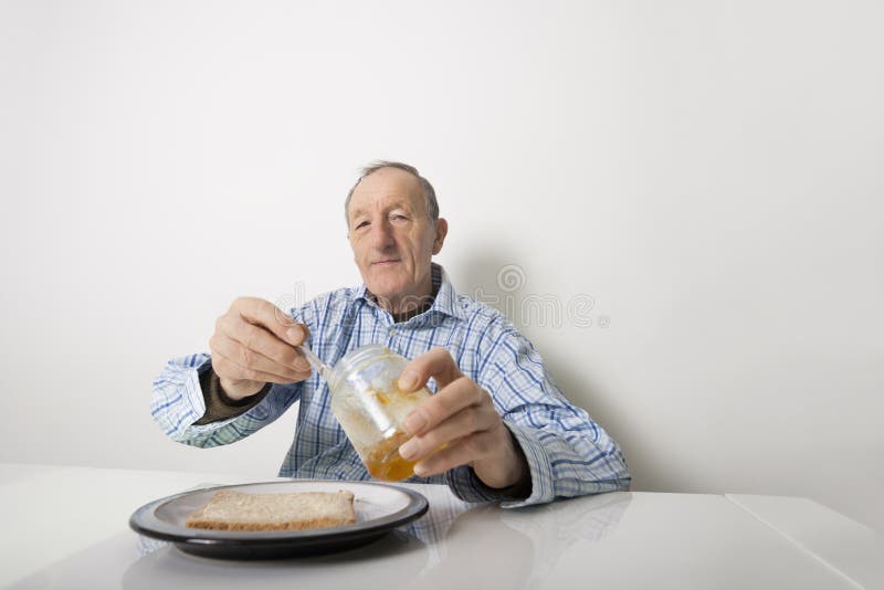 Portrait of senior man preparing slice of bread and marmalade at table stock photo