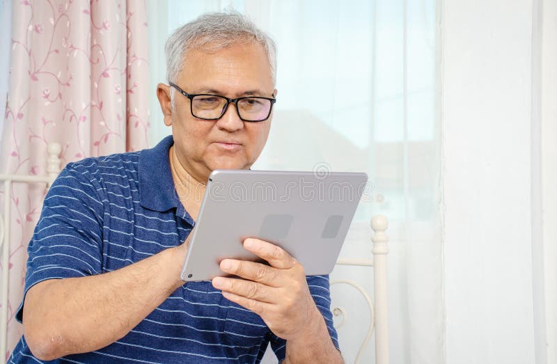 Portrait of senior man sitting at sofa at home and reading news on digital tablet stock photo Portrait of senior man sitting at sofa at home and reading news on digital tablet stock photo