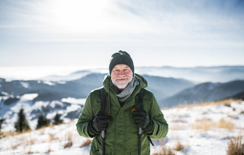 Portrét staršieho muža stojaceho v zasneženej zimnej prírode, pri pohľade na fotoaparát.