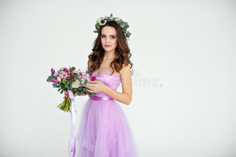 Portrait of sensual beautiful brunette girl in purple dress, wreath and bouquet of flowers. Beauty. White background