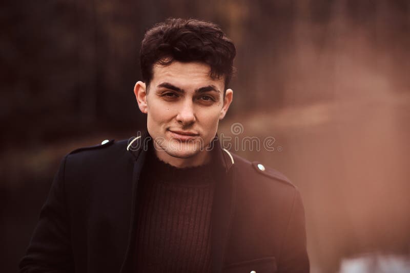 Portrait of a sensual young man wearing a black coat in the autumn forest. stock photo Portrait of a sensual young man wearing a black coat in the autumn forest. stock photo