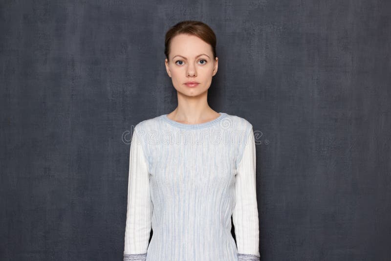 Portrait of serious focused young woman holding arms along body